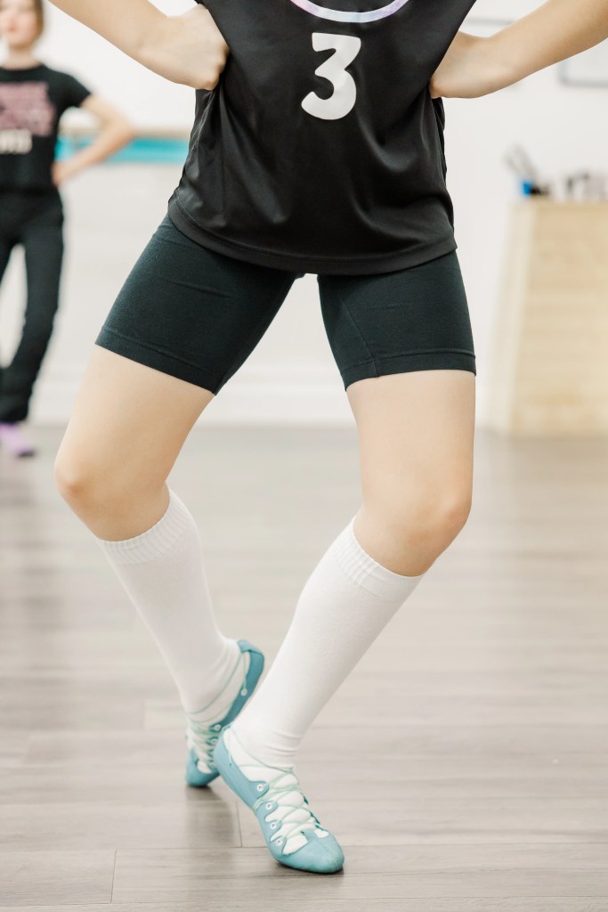 A highland dancer wearing black, white socks, and blue ghillies demonstrates a position. Saorsa Studio offers Highland Dance classes for ages 1 to adult in Fredericton, New Brunswick.