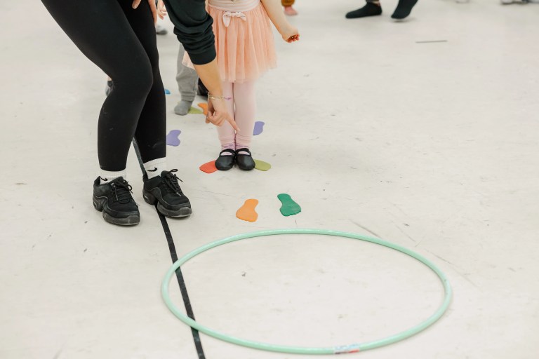 A person wearing black helps guide a child wearing pink to jump around colourful dance class obstacles. Saorsa Studio offers Highland Dance classes for ages 1 to adult in Fredericton, New Brunswick.