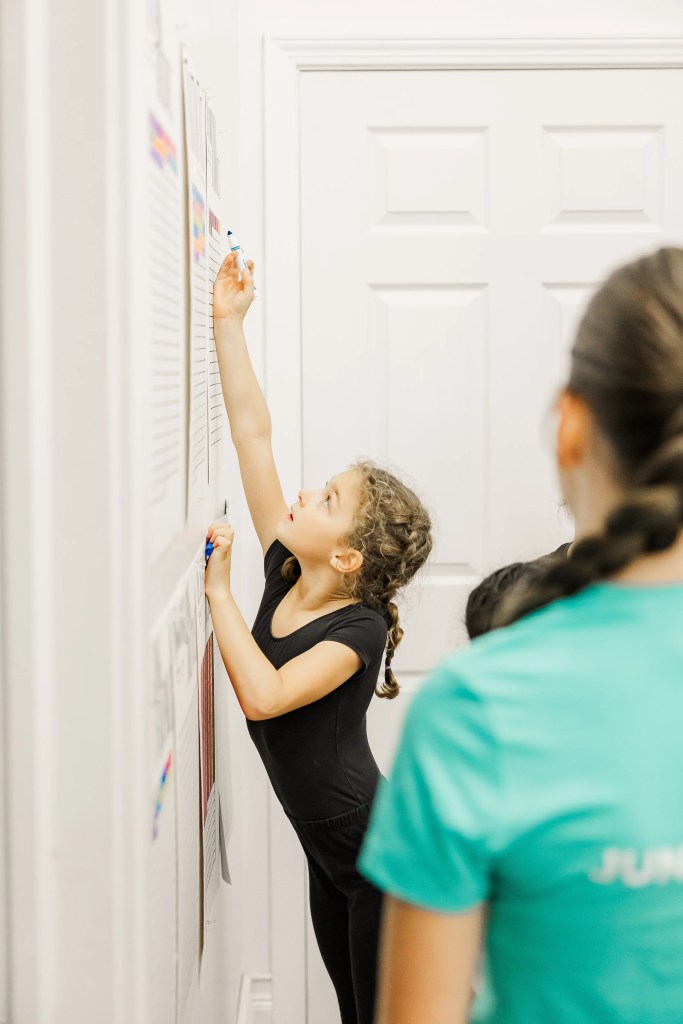 A child in a black dance body suit reaches to colour on a sheet on the wall with a marker. Saorsa Studio offers Highland Dance classes for ages 1 to adult in Fredericton, New Brunswick.