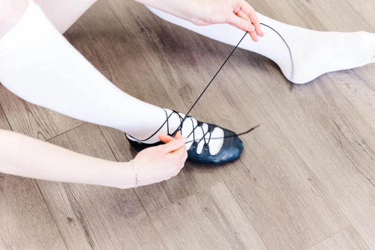 A highland dancer sits on the floor wearing white socks and tying their black leather shoe. Saorsa Studio offers Highland Dance classes for ages 1 to adult in Fredericton, New Brunswick.